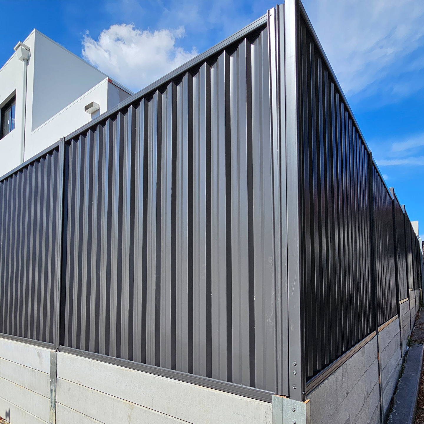 Modern Sydney property featuring a corrugated metal fence with vertical ridges mounted on a concrete base beside a contemporary white building.