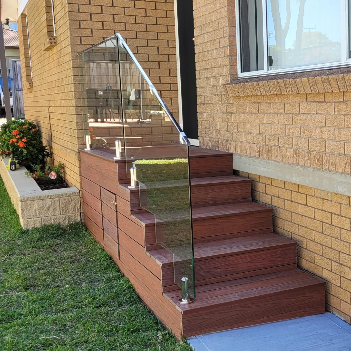 Modern Sydney exterior featuring timber steps with a sleek glass balustrade beside a landscaped garden bed.