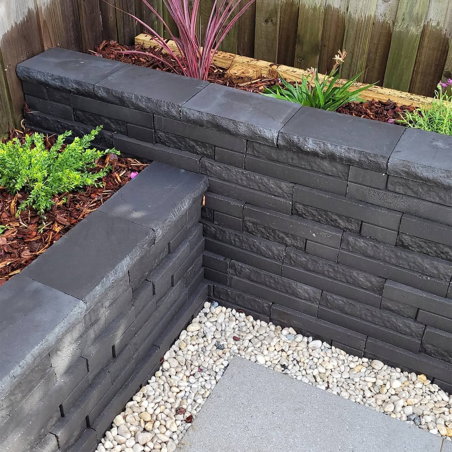 Modern Sydney garden featuring dark textured masonry blocks forming a clean L‑shaped retaining wall beside mulched planting.