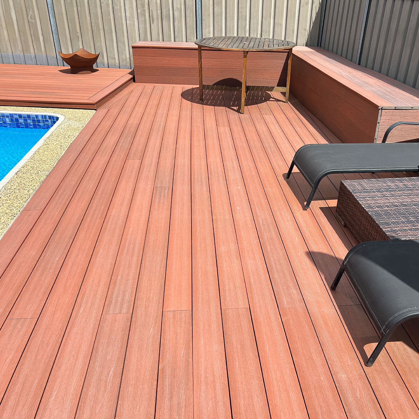 Modern Sydney poolside area featuring composite decking, lounge chairs, outdoor tables and a clean tiled pool edge.